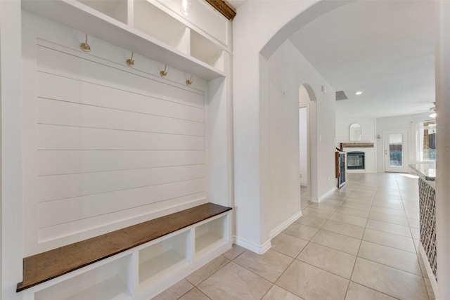 mudroom featuring ceiling fan, a large fireplace, and light tile patterned floors