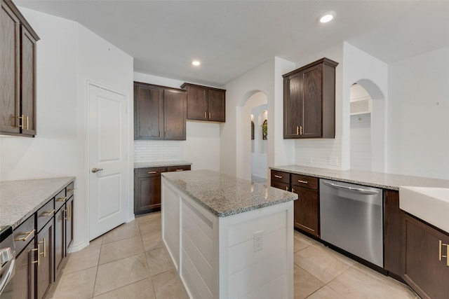 kitchen with light stone countertops, backsplash, dark brown cabinets, light tile patterned floors, and dishwasher