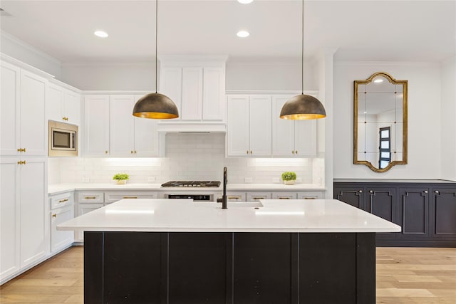 kitchen with white cabinets, decorative backsplash, stainless steel appliances, and a center island with sink