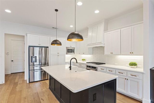 kitchen featuring a center island with sink, sink, appliances with stainless steel finishes, decorative light fixtures, and white cabinetry