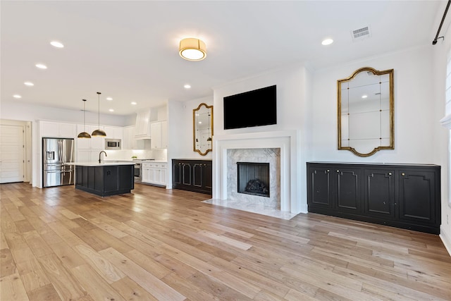 unfurnished living room featuring sink, light wood-type flooring, and a premium fireplace