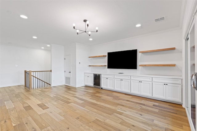 unfurnished living room featuring a chandelier, beverage cooler, light wood-type flooring, and ornamental molding