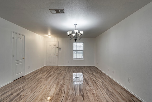 spare room with a chandelier, a textured ceiling, and light hardwood / wood-style flooring