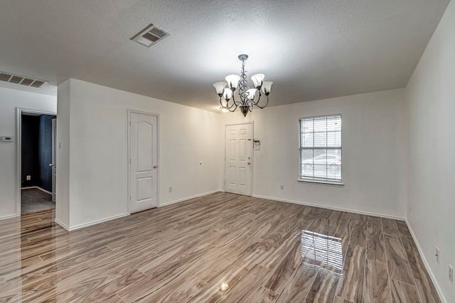 spare room with hardwood / wood-style floors, a textured ceiling, and a notable chandelier