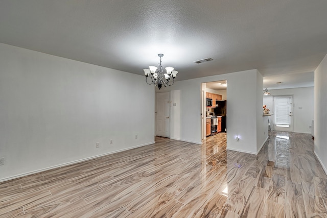 spare room featuring a chandelier, light hardwood / wood-style floors, and a textured ceiling