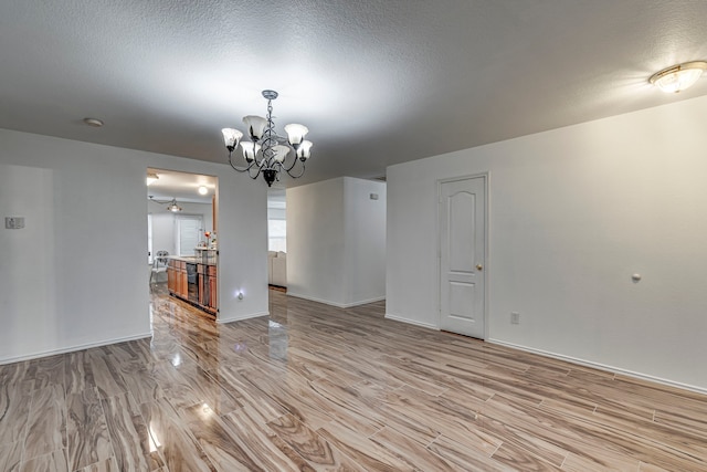 empty room with a chandelier, a textured ceiling, light hardwood / wood-style floors, and beverage cooler