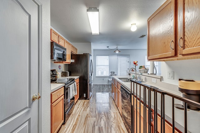 kitchen with black appliances, light wood-type flooring, sink, and a textured ceiling