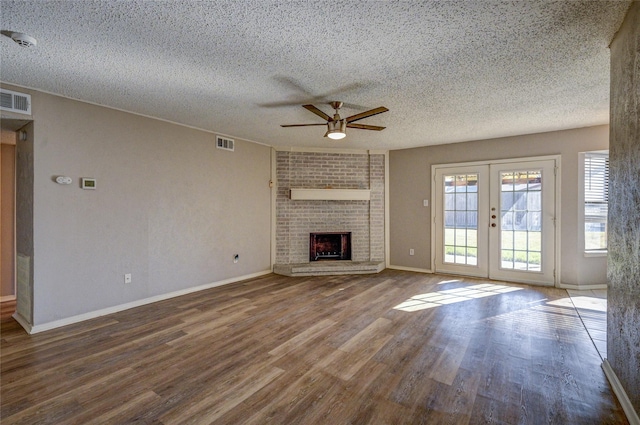 unfurnished living room with ceiling fan, french doors, a brick fireplace, a textured ceiling, and hardwood / wood-style flooring