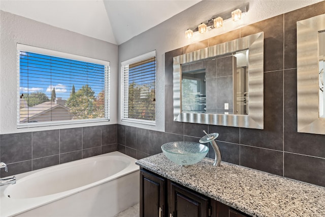 bathroom featuring a bathing tub, vanity, a healthy amount of sunlight, and lofted ceiling