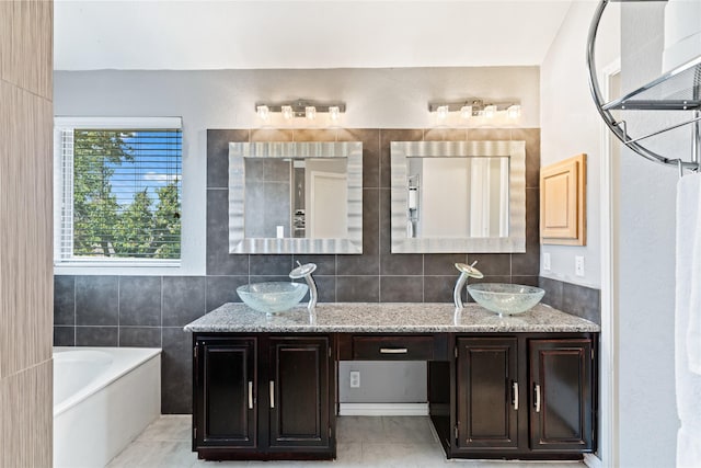 bathroom featuring tile patterned floors, a bathing tub, vanity, and tile walls