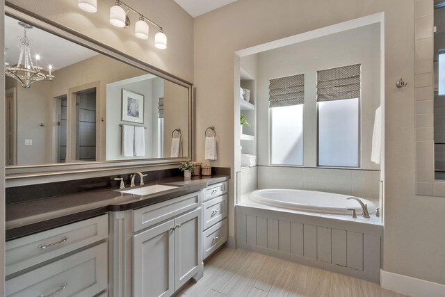 bathroom with vanity, plenty of natural light, tiled bath, and a chandelier