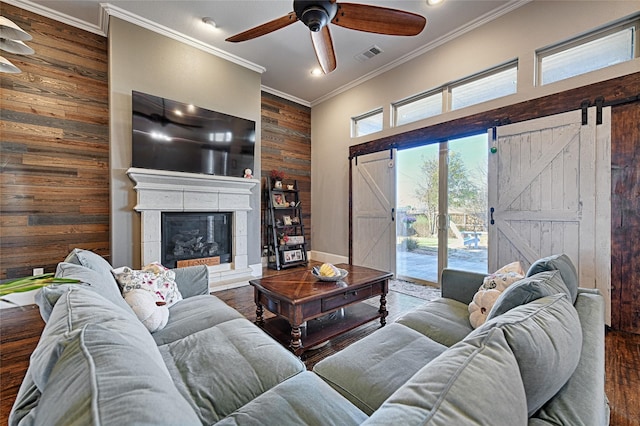 living room with crown molding, wood-type flooring, a barn door, a fireplace, and wood walls