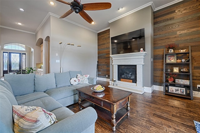 living room with ceiling fan, ornamental molding, dark wood-type flooring, and wooden walls