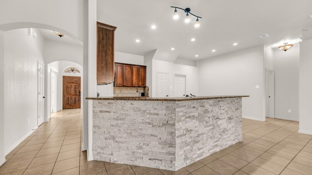 kitchen featuring arched walkways, light tile patterned floors, recessed lighting, tasteful backsplash, and dark stone countertops