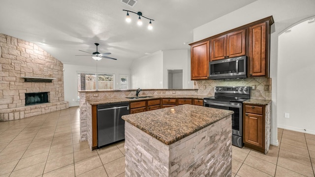 kitchen featuring light tile patterned floors, stainless steel appliances, decorative backsplash, a stone fireplace, and a peninsula