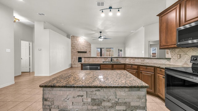 kitchen featuring a stone fireplace, stainless steel appliances, a sink, visible vents, and decorative backsplash