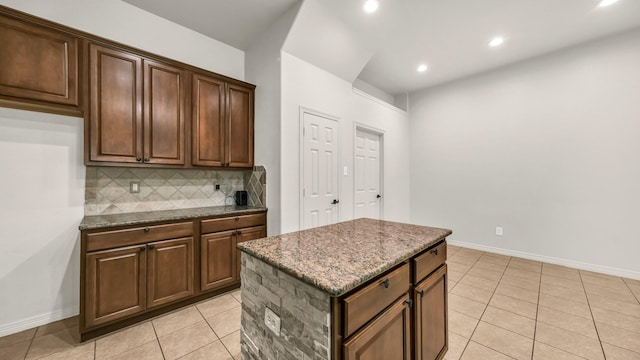 kitchen with light tile patterned floors, tasteful backsplash, baseboards, dark stone countertops, and a center island