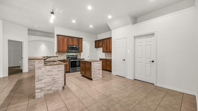 kitchen with sink, stainless steel appliances, light tile patterned floors, backsplash, and a kitchen island