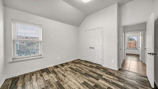 unfurnished bedroom with vaulted ceiling, a closet, wood finished floors, and baseboards