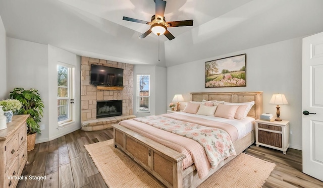 bedroom featuring vaulted ceiling, a stone fireplace, multiple windows, and wood finished floors