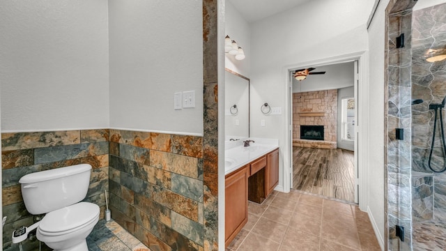 bathroom featuring vanity, tile walls, hardwood / wood-style floors, toilet, and a stone fireplace