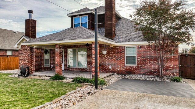 rear view of house with brick siding, a chimney, a shingled roof, a patio area, and fence