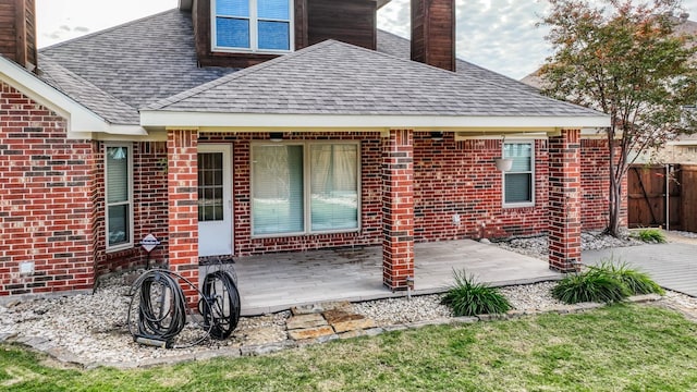 rear view of house featuring brick siding, roof with shingles, a patio area, and fence