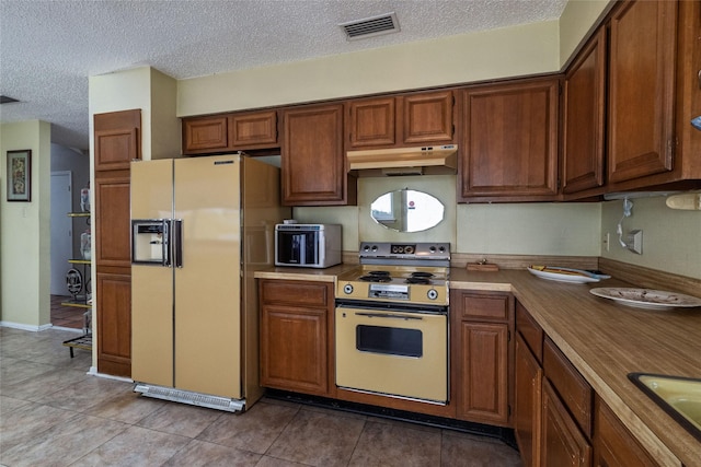 kitchen featuring refrigerator with ice dispenser, sink, range, a textured ceiling, and light tile patterned flooring