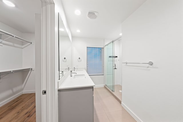 full bath featuring a walk in closet, a stall shower, a sink, double vanity, and baseboards