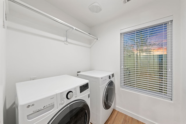 clothes washing area with laundry area, washer and dryer, light wood-type flooring, and baseboards