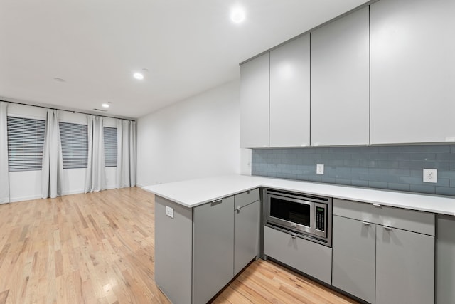 kitchen featuring kitchen peninsula, decorative backsplash, light wood-type flooring, and stainless steel microwave