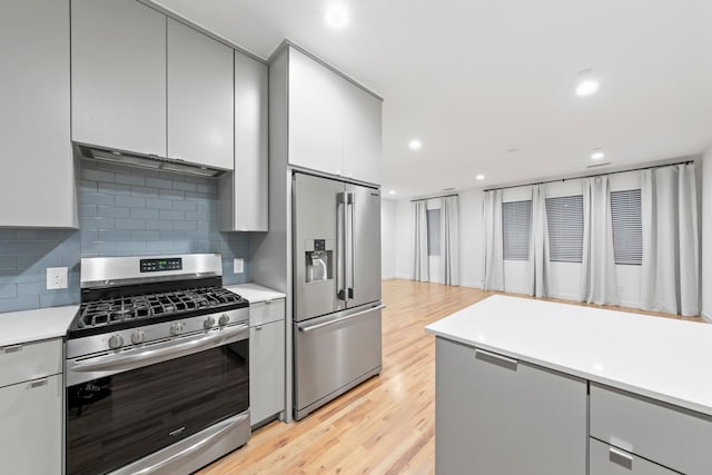 kitchen featuring light wood finished floors, tasteful backsplash, light countertops, gray cabinets, and stainless steel appliances