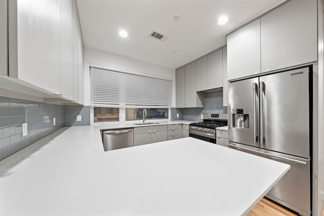 kitchen featuring kitchen peninsula, appliances with stainless steel finishes, tasteful backsplash, sink, and light hardwood / wood-style flooring