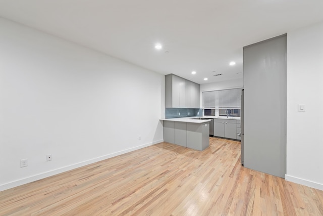 kitchen with sink, backsplash, kitchen peninsula, a breakfast bar area, and light wood-type flooring