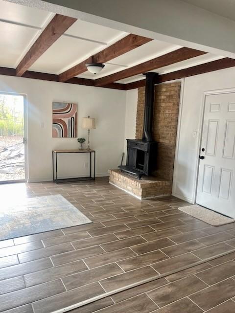 unfurnished living room featuring beam ceiling and a wood stove