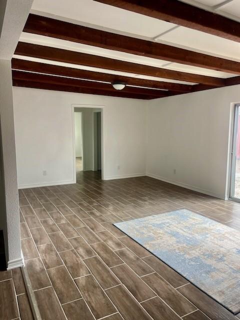 empty room featuring wood-type flooring and beamed ceiling