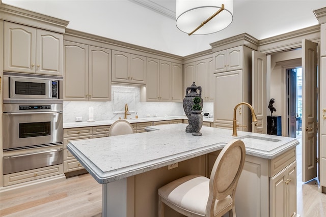 kitchen featuring a center island with sink, sink, light wood-type flooring, light stone counters, and stainless steel appliances