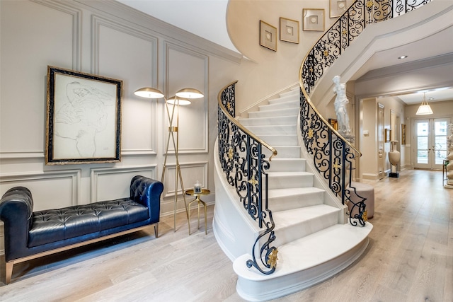 staircase featuring french doors, a towering ceiling, ornamental molding, and hardwood / wood-style flooring