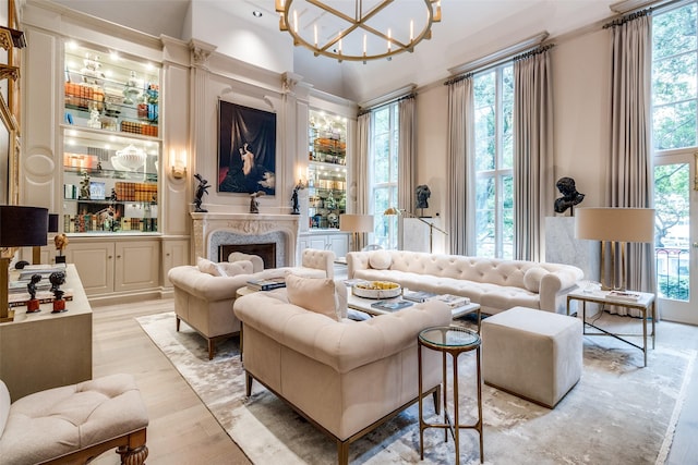 living room featuring a chandelier, light hardwood / wood-style floors, a healthy amount of sunlight, and a high end fireplace