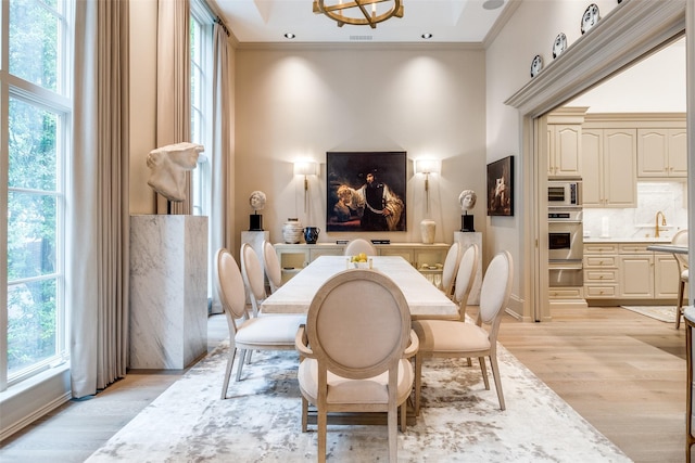 dining room featuring plenty of natural light, light hardwood / wood-style floors, a towering ceiling, and crown molding