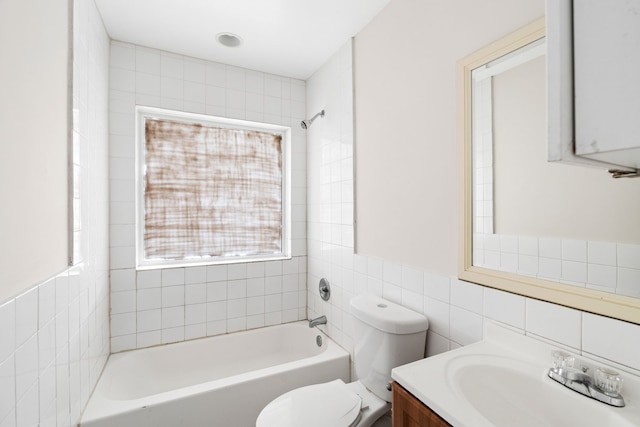 full bathroom with tiled shower / bath, vanity, tile walls, and toilet