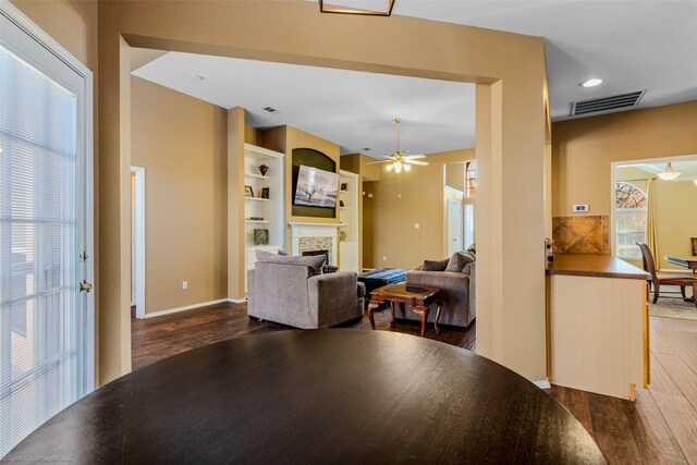 dining area featuring a fireplace, ceiling fan, and dark wood-type flooring