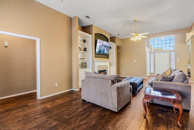 living room featuring ceiling fan, a stone fireplace, a towering ceiling, and dark wood-type flooring