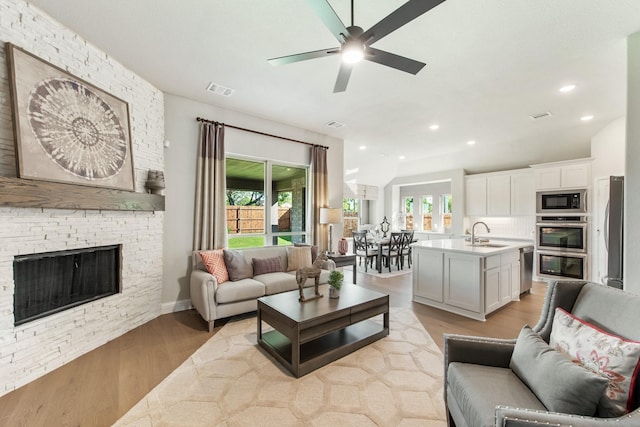 living room featuring ceiling fan, sink, a fireplace, and light hardwood / wood-style floors