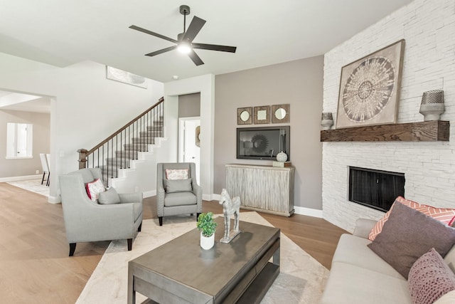 living room with hardwood / wood-style flooring, a stone fireplace, and ceiling fan