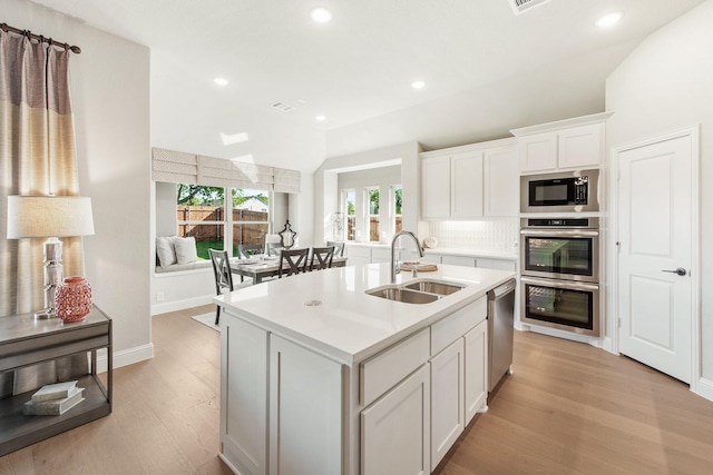 kitchen featuring sink, white cabinetry, light wood-type flooring, appliances with stainless steel finishes, and an island with sink