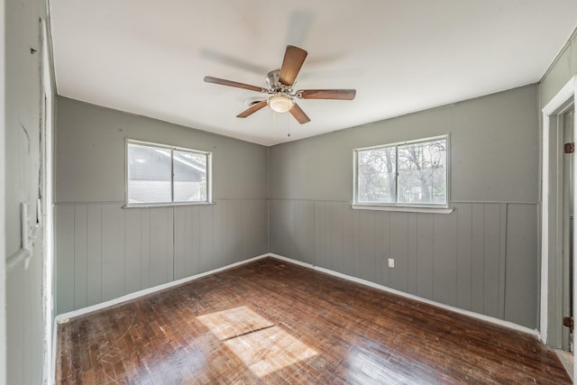 empty room with ceiling fan, plenty of natural light, dark wood-type flooring, and wooden walls