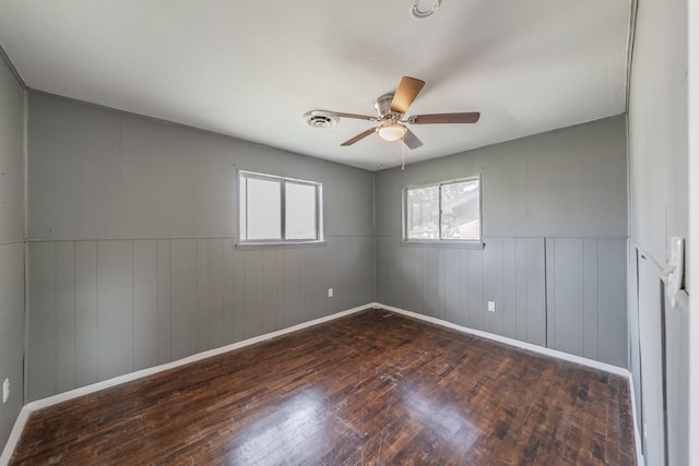 unfurnished room with a wealth of natural light, wood walls, ceiling fan, and dark hardwood / wood-style floors