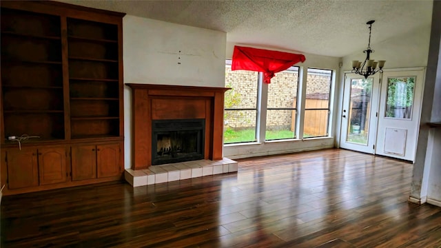 unfurnished living room with a textured ceiling, a tiled fireplace, dark hardwood / wood-style floors, and an inviting chandelier