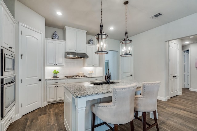 kitchen featuring a kitchen island with sink, hanging light fixtures, dark hardwood / wood-style floors, white cabinetry, and stainless steel appliances